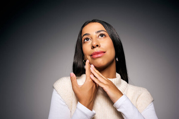 The young woman gazes upward with a serene expression, hands delicately resting on her face.