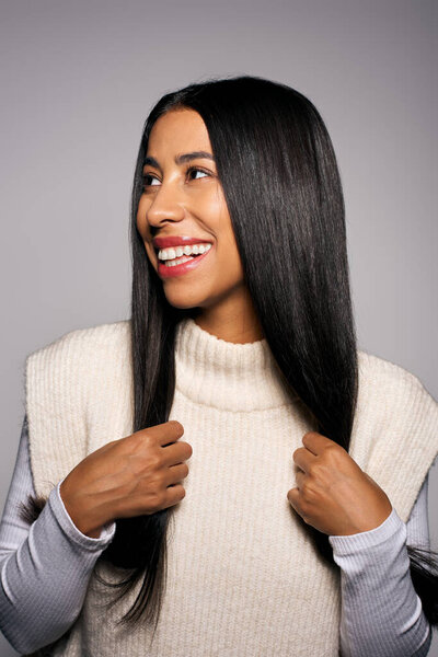 Женщина выражает счастье и уверенность, демонстрируя свои длинные волосы в уютном свитере.