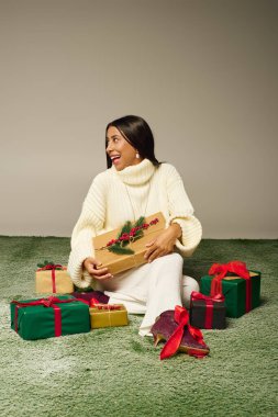 Neşeli bir kadın renkli tatil paketleriyle çevrili bir hediyeyi kucaklıyor..