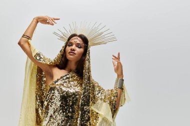 Zarif bir Afrikalı Amerikalı kadın göz kamaştırıcı altın bir elbiseyle süslenmiş. Duruşuyla hareket ediyor, güzelliğini gösteriyor..