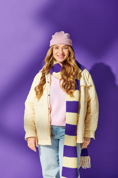 A joyful young plus size woman stands warmly dressed in a stylish winter outfit while smiling.