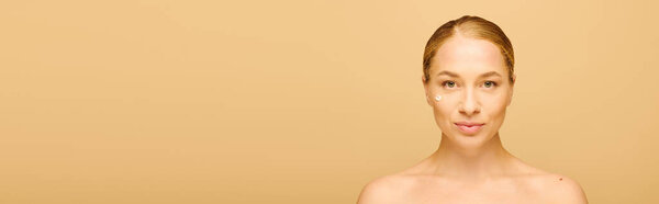 A confident young woman enhances her beauty with skincare in a soft, warm toned space.