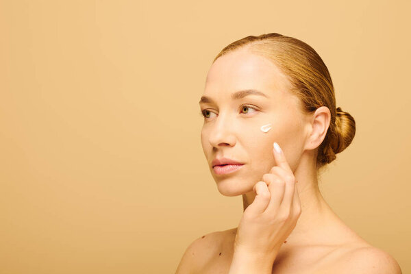 A young beautiful plus size woman tenderly applies cream to her face, showcasing her glowing skin.