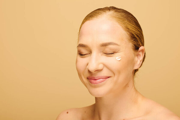 A young plus size woman smiles with cream on her face, radiating happiness.