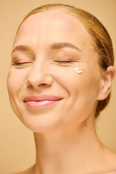 Молодая женщина плюс размер тихо улыбается, позируя со сливками на щеке в теплом пространстве.