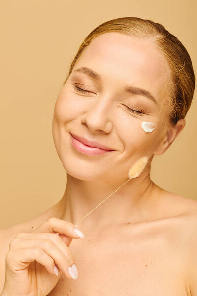 Молодая женщина нежно улыбается, нанося крем на лицо в теплой и уютной атмосфере..