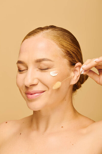 Молодая красивая женщина плюс размер радостно применяет фундамент, повышая ее естественное сияние.