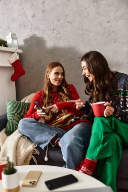 Noel 'i ve yeni yılı evde kutlarken rahat kazaklı iki kız arkadaş neşe ve kahkahayı paylaşıyor..