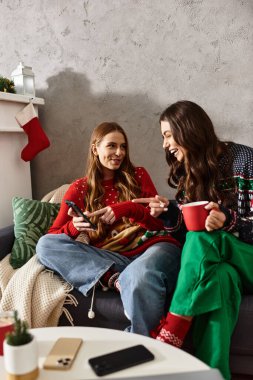 Two girlfriends in cozy sweaters share joy and laughter while celebrating Christmas and New Year at home. clipart