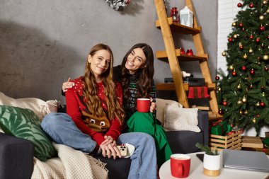 Two girlfriends enjoy each other's company in cozy sweaters while celebrating the holiday season at home. clipart