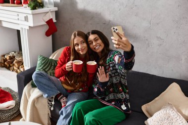 İki kız arkadaş tatil neşesini rahat kazaklarla paylaşıyor, sıcak içkilerini yudumluyor ve evde anılarını yakalıyorlar..