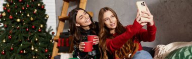 Two girlfriends in cozy sweaters enjoy festive drinks while celebrating Christmas and New Year together. clipart