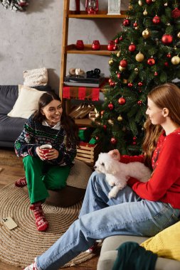 Kazaklı iki arkadaş tatil sezonunun tadını çıkarıyorlar. Evde Noel ağacının yanında şirin bir köpekle..