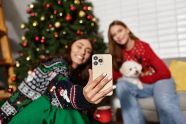 Şenlikli kazaklı iki arkadaş şirin Bichon Frise köpekleri ile rahat bir Noel buluşmasının tadını çıkarıyorlar..