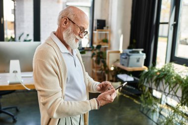 Düzgün giyimli üst düzey bir yönetici telefonuyla parlak ve modern bir çalışma alanında etkileşime girer..