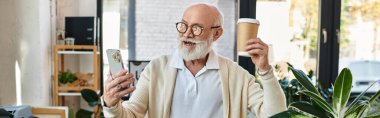 A bearded senior manager in smart casual attire is cheerfully video chatting while holding coffee. clipart