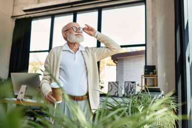 A distinguished senior businessman with a beard stands in a stylish office, savoring his coffee while reflecting. clipart