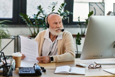 İyi giyimli, sakallı kıdemli bir işadamı, çağdaş bir ofis masasındaki görevlere odaklanır..