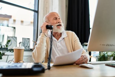 A well-dressed senior businessman with a beard chats on the phone while reviewing documents at his desk. clipart