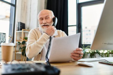 Üst düzey işadamı modern bir çalışma alanında telefonla konuşurken belgeleri gözden geçiriyor..