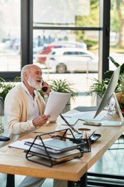 A senior businessman in smart casual attire makes a phone call while reviewing documents, surrounded by greenery. clipart