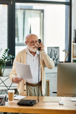 Sakallı şık bir kıdemli işadamı önemli evrakları incelerken telefonla iletişim kuruyor..