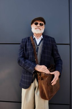 Güz boyunca şık giyinmiş, gösterişli bir binanın yanında sakallı, modaya uygun, son sınıf öğrencisi duruyor..