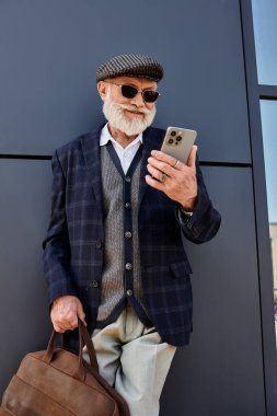 Sakallı, iyi giyimli bir son sınıf öğrencisi, güz havasının tadını çıkarırken akıllı telefonunu kullanıyor..