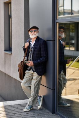 Şık, son sınıf öğrencisi bir adam güz mevsiminde şık bir binanın yanında duruyor ve şık ve rahat tarzını sergiliyor..