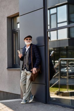 Modern bir binanın yanında kendine güveni tam, şık kıyafetleriyle çekici bir adam duruyor..