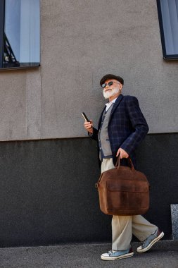 Şık bir son sınıf öğrencisi, şık bir sonbahar kıyafeti giymiş, modern bir binanın yanında rahatça dolaşır..