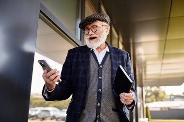 Sakallı son sınıf öğrencisi, bir sonbahar günü şık bir kıyafet giyerken telefonunu kullanmaktan zevk alır..