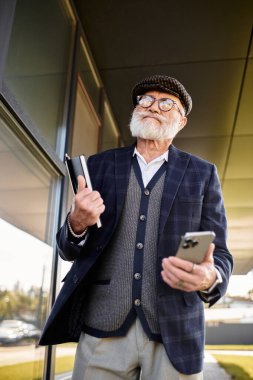 Şık bir kıdemli adam, sonbaharda şık bir modern binanın önünde kareli ceket ve düz şapka giyer..