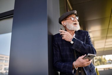 Süslü ceketli ve düz şapkalı şık bir son sınıf öğrencisi, sonbaharı kucaklayan gösterişli bir binaya yaslanıyor..