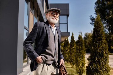 Sakallı, modaya uygun, son sınıf öğrencisi modern bir binanın yanında duruyor ve sonbahar güneşinin tadını çıkarıyor..