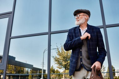 İyi bakımlı sakallı kıdemli bir adam şık kıyafetini şık bir şehir arka planına karşı sergiliyor..