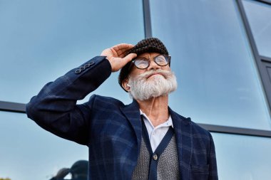 Şık bir kıdemli adam güler ve şapkasını çıkartır. Sonbaharda çağdaş bir binanın yanında güvenle durur..