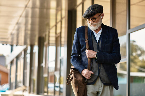 A fashionable senior man with a beard stands elegantly outside a modern building on an autumn day.