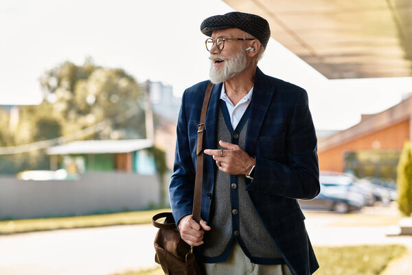 A dapper senior man with a beard and a cap casually leans near a contemporary building on an autumn day.