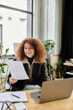 A joyful woman reads through important documents, immersed in her work at a stylish desk. clipart