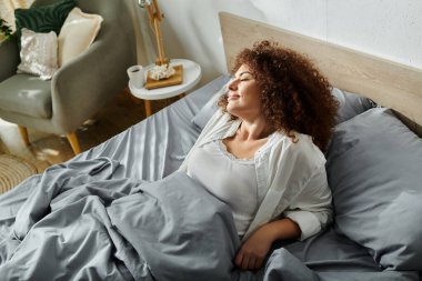 Bir kadın, rahat bir atmosfer ve yumuşak tekstil ile çevrili yatağında huzur içinde uzanıyor..