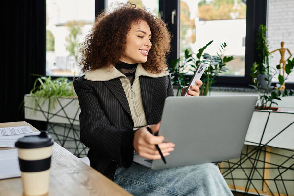 A woman engages with her phone while focused on her laptop surrounded by plants.