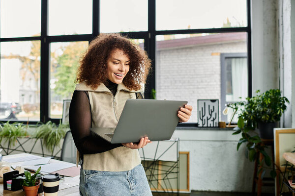 Молодая женщина улыбается, взаимодействуя со своим ноутбуком в шикарном рабочем месте, заполненном растениями.