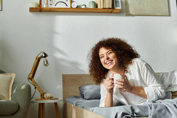 Веселая женщина наслаждается своим напитком, излучая тепло в спокойной, мягко освещенной спальне.