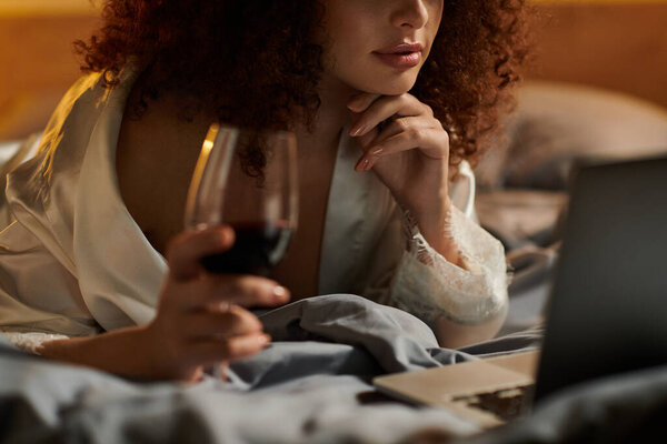 The woman savors her wine as she engrosses herself in a late night online task.