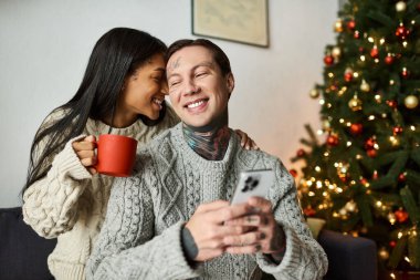 A couple enjoys each others company while sipping warm drinks and sharing smiles during Christmas. clipart