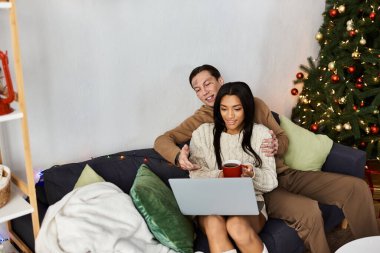 Sevgi dolu bir çift kanepede dinlenir, tatil anlarını dizüstü bilgisayarlarına bakarak paylaşır..