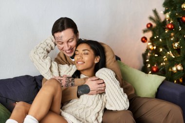 A couple enjoys each others company by the Christmas tree, radiating love and warmth. clipart