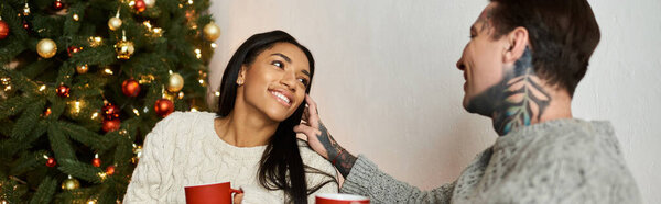 A couple enjoys a warm moment at home, sharing smiles and hot beverages during Christmas.
