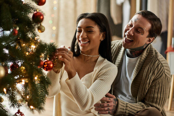 Loving partners share laughter while decorating their festive Christmas tree at home.